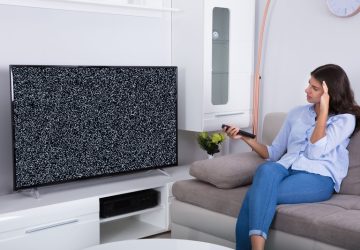 La TV si sente ma non si vede, donna sul divano guarda triste la tv che non si vede